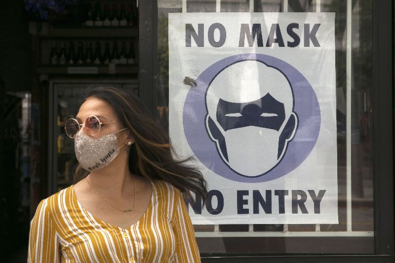 A woman walks out of a liquor store past a sign requesting its customers to wear a mask Tuesday in Santa Monica, Calif.  (Photo by Jae C. Hong/AP Photo)